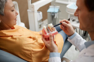 Closeup of male dentist holding tooth model while explaining dental implant surgery to a new patient in a dental clinic